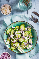 Diet salad of cucumbers, red onions and ricotta on a plate on the table top and vertical view