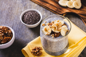 Chia seeds pudding with fresh banana and walnuts in a glass on the table