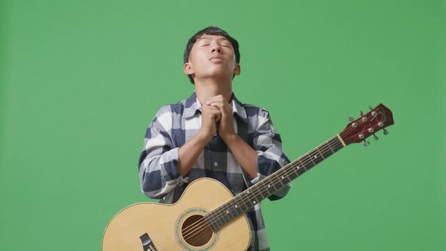 Asian Teenager With Guitar Pray For Something On Green Screen Background
