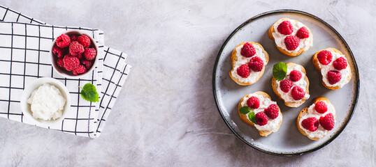 Sweet bruschettas with curd cheese and raspberries on a plate top view web banner