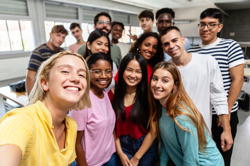 Diverse group of young student people taking selfie at university classroom. Millennial classmates posing with male teacher for self photo together. Education and community concept.