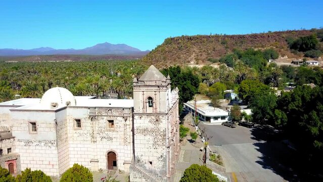 Aerial Shot Of Mission San Ignacio Kadakaaman By Road, Drone Descending Forward Over Catholic Church On Sunny Day - Baja California, Mexico