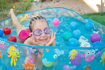 a girl in swimming goggles laughs close-up and swims with water splashes and plastic bright colored...