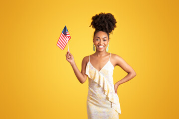 Smiling millennial african american lady showing USA flag, isolated on yellow background