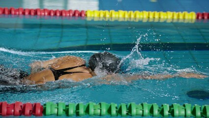 Slowmotion of powerful and persistent professional female swimmer swimming front crawl, tracking shot. Endurance, effort, and focus concept.