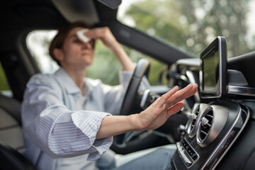 Woman drives car with broken air conditioning in hot summer weather wipes sweat on forehead with...