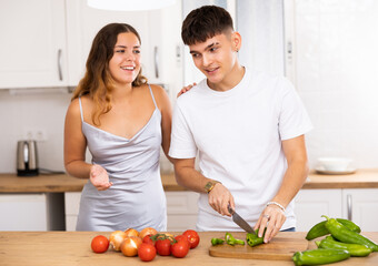 Woman preparing vegetable salad and communicating with her husband in modern kitchen