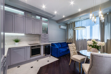 Stylish interior of a small studio apartment. The room is decorated in bright colors. .A kitchen set, a dining table with chairs and a bright blue sofa.