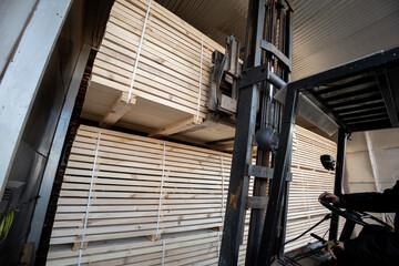 A diesel forklift loads freshly sawn pine logs, girders, bars, beams, bars, boards into a drying...