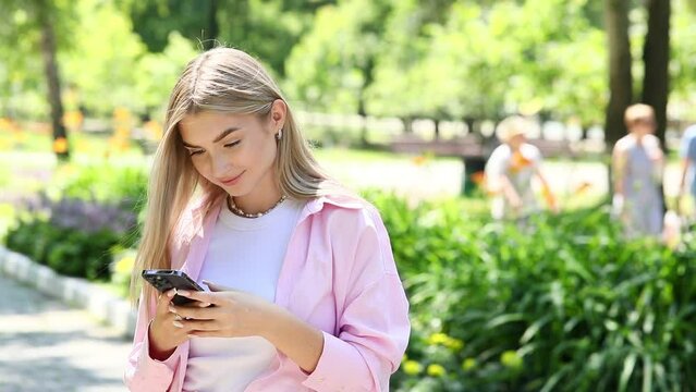 Young beautiful blonde girl with a mobile phone in a summer park
