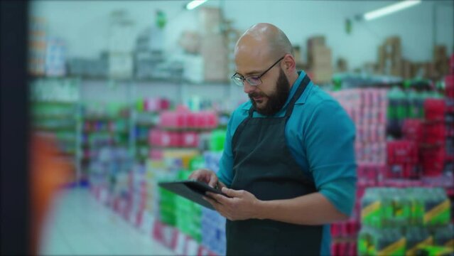 Male Grocery Store Employee with Apron Browsing Inventory on Tablet