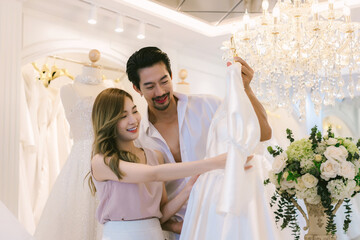 Bride and groom choosing wedding dress in shop. Bride and groom choose dress and try to fitting in modern wedding studio.