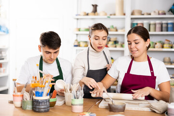 Interested young man and woman in aprons making handmade cups of row clay material and master...