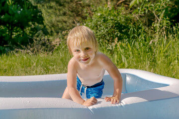 Cute blond little toddler kid boy playing splashing water in inflatable pool on private backyard during heat.Summer recreational holidays with children,Child healthcare time