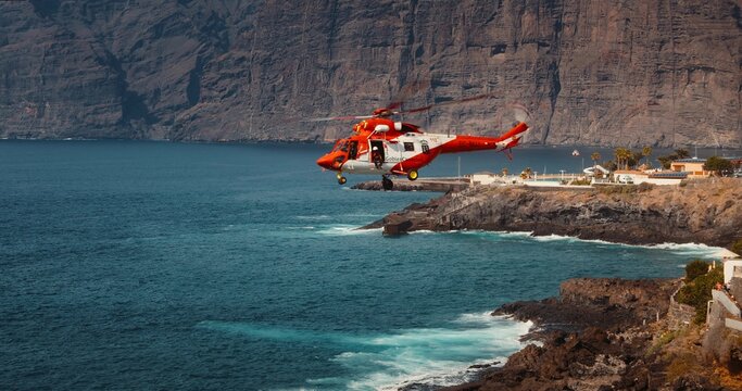 TENERIFE, CANARY ISLANDS, SPAIN, 2023 April: Rescue helicopter flies over a stormy ocean near rocky coastline. Charco de Isla Cangrejo. Puerto Santiago town.