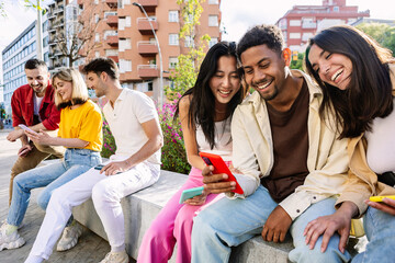 Young group of multi-ethnic net generation friends having fun using cellphones outdoors. Smiling...