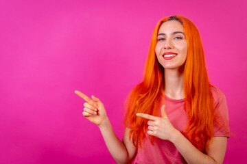 Redhead woman in studio photography making the gesture of pointing on a pink background