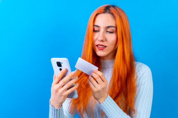 Redhead woman in studio photography online payment with mobile on a blue background