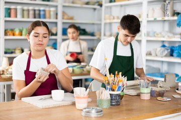 Fototapeta premium Young man and young woman making pottery from clay in workshop