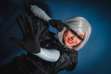 Portrait of cosplay woman in a black costume and a white wig in studio on a blue background