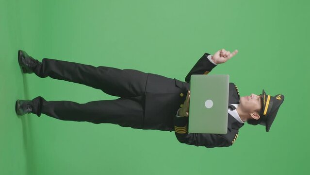 Full Body Of Asian Man Pilot Using A Laptop And Pointing To Side While Standing In The Green Screen Background Studio
