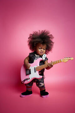 Little baby girl playing electric guitar against  light pastel pink background. Concept of happiness, good music, children's party, birthday celebrations. Generative AI.