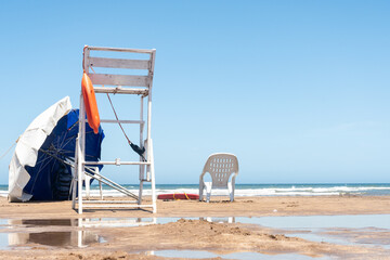 Empty lifeguard station on the beach with chair and umbrella. Copy space.