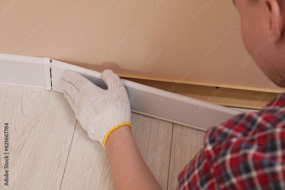 Sticker Man installing plinth on laminated floor in room, closeup