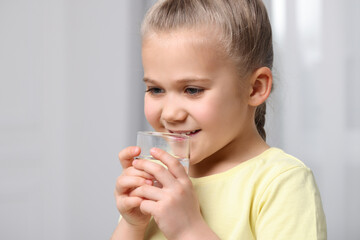 Little girl drinking fresh water from glass indoors