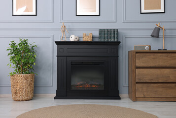 Black stylish fireplace between potted plant and chest of drawers in cosy living room