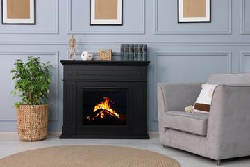 Black stylish fireplace near armchair and potted plant in cosy living room