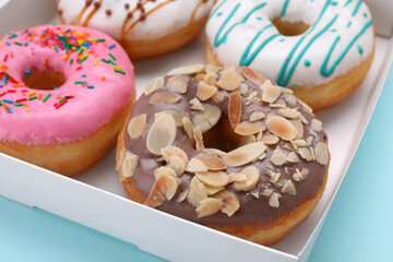 Box with different tasty glazed donuts on light blue background, closeup