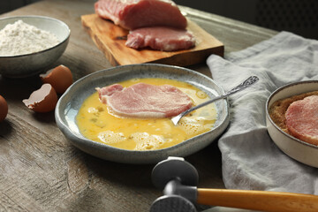 Cooking schnitzel. Raw pork chop in eggs, meat mallet and ingredients on wooden table