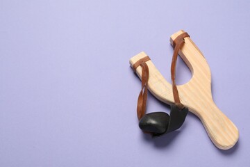 Wooden slingshot with pebble on violet background, top view. Space for text