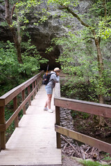 woman tourist in a hat with a backpack stands on a wooden bridge across a mountain river in the forest.