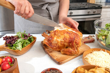Woman cuts into a roast chicken for making Caesar salad. Hands and knife close-up.