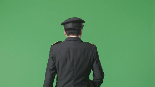 Back View Of Asian Man Pilot Holding A Tablet While Walking In The Green Screen Background Studio
