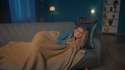 Tired sleepy woman fell asleep while watching TV. A woman sleeps, covered with a blanket, lying on...