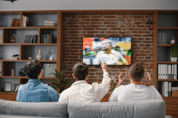 Back view of men watching a football game on tv and sitting on a sofa