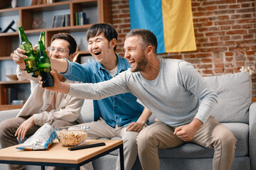 Three men watching a football game on tv and drinking a beer