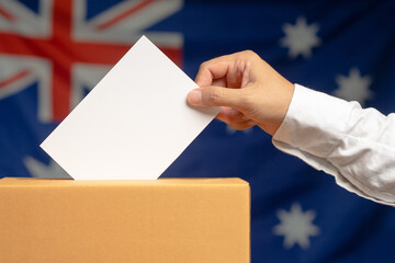 Hand voter holding ballot paper putting into the voting box at place election against the Australia...