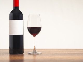 A Wine bottle and a glass of red wine are on the table against a gray background.