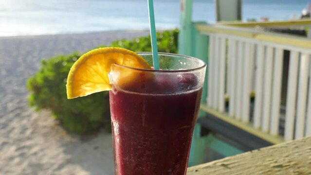Tropical refreshing frozen fruity drink in drinking glass with lemon wedge and beach vacation resort out of focus in background