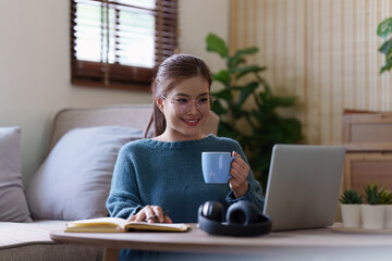 Young asian relaxed smiling pretty woman relaxing with laptop at home. Female feeling joy enjoying with mobile phone on cozy couch