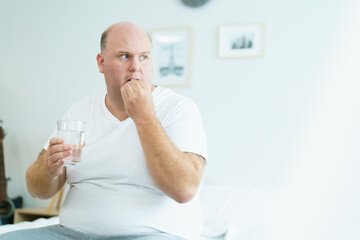 Unwell caucasian man got a sickness, oversize fat man taking a pills and drinking water in a...
