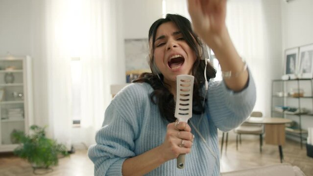 Portrait of happy crazy carefree latin american girl dancing and singing in hair brush mic having fun in apartment. Slow motion funny hispanic woman dancing with hands. Joyful people lifestyle concept