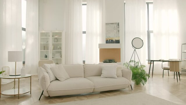 Cinematic view stylish urban loft apartment with large windows, high ceiling. Dolly shot home interior design. Modern clean living room with soft and cozy sofa with pillows. Home sweet home background