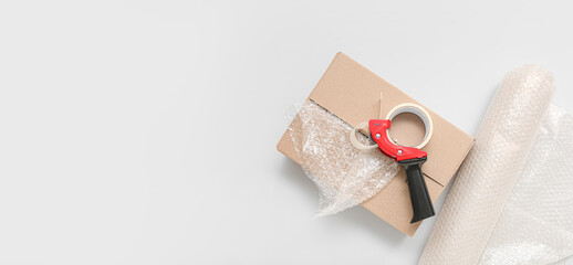 Packing tape dispenser, cardboard box and roll of bubble wrap on light background with space for...