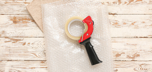 Packing tape dispenser, bubble wrap and paper on white wooden background