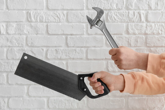 Worker with wrench and handsaw on white brick background
